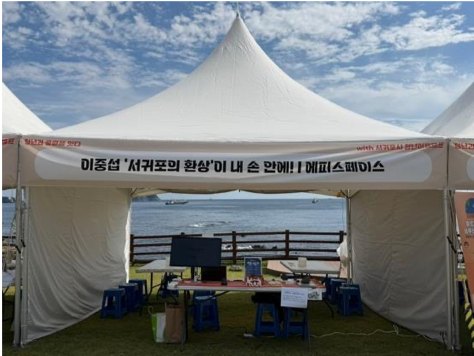 바다를 배경으로 선 에피스페이스 천막. 깃에는 서귀포의 환상이 내 손 안에라고 적혀 있다